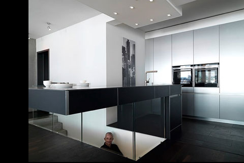 modern metalic kitchen front, cooking area dark grey surface, glass front of staircase to the lower floor