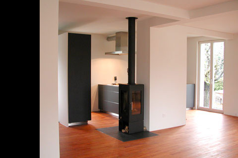 parquet floor, dark elegant wood burning stove, modern kitchen behind